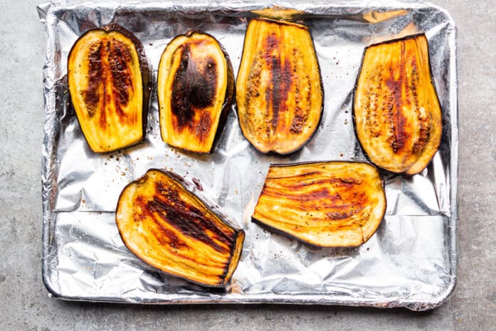 sheet pan covered in aluminum foil with roasted eggplant halves on top, authentic baba ganoush recipe