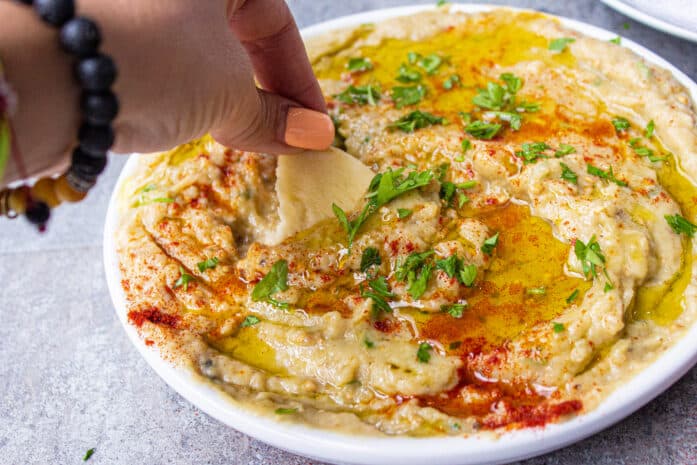 woman dipping pita into mediterranean eggplant dip