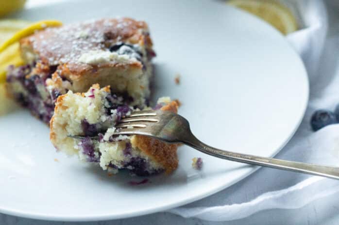 slice of blueberry yogurt cake sitting on a plate with a fork holding the first bite